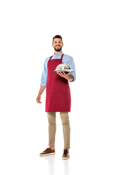 Camarero sonriente guapo sosteniendo bandeja de metal y cubierta de plato sobre fondo blanco - foto de stock