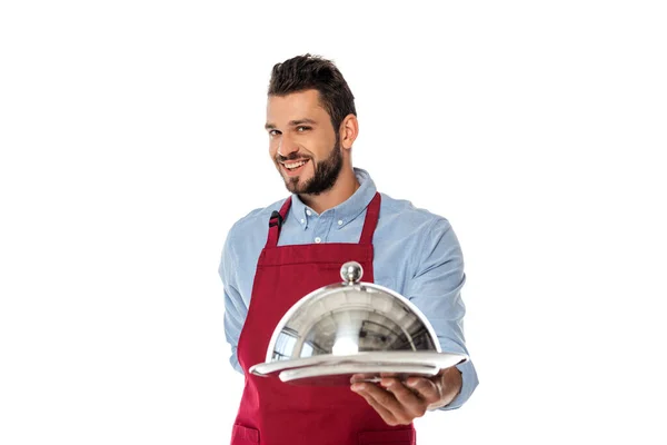 Вибірковий фокус красивого усміхненого офіціанта, що тримає лоток і кришку посуду ізольовано на білому — стокове фото