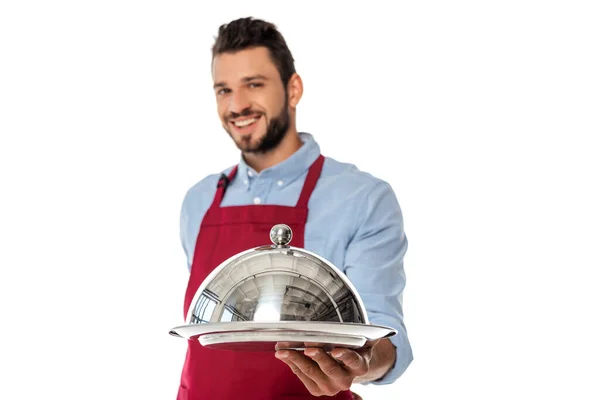 Focus selettivo del cameriere barbuto sorridente che tiene il vassoio e del cloche isolato sul bianco — Foto stock