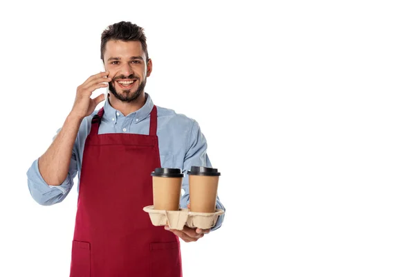 Smiling waiter talking on smartphone while holding paper cups isolated on white — Stock Photo