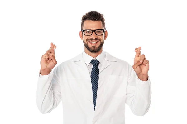Красивый улыбающийся доктор со скрещенными пальцами смотрит на камеру, изолированную на белом — стоковое фото