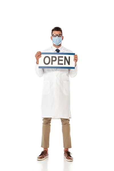 Молодой врач в белом халате и медицинской маске держит вывеску с открытыми буквами на белом фоне — стоковое фото