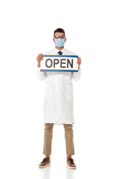 Giovane medico in cappotto bianco e maschera medica con cartello con scritte aperte su sfondo bianco — Foto stock