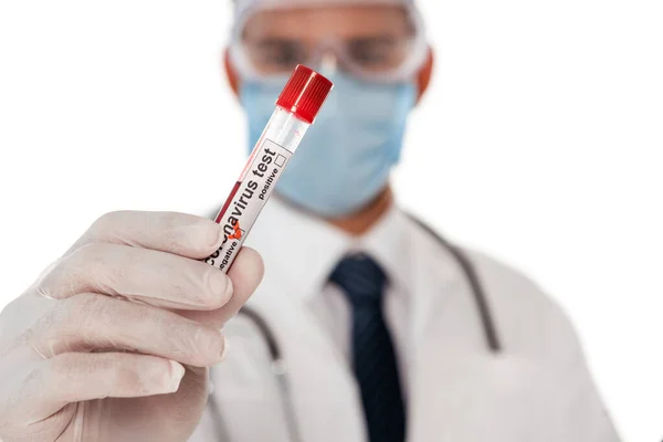 Concentration sélective du médecin dans le masque de sécurité et les lunettes montrant tube à essai avec échantillon de sang et lettrage coronavirus isolé sur blanc — Photo de stock