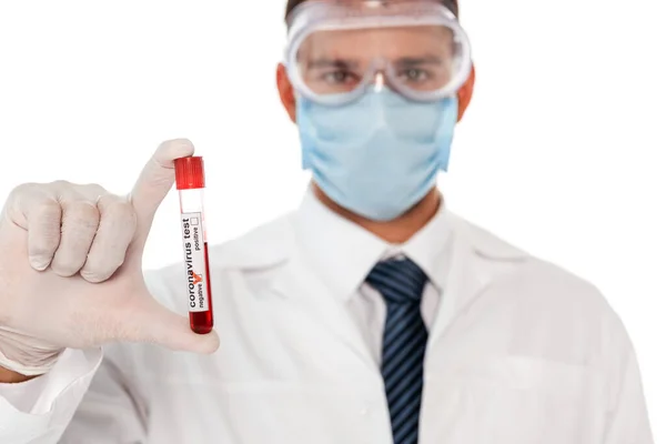 Concentration sélective du médecin dans le masque protecteur et les lunettes tenant le tube à essai avec échantillon de sang et lettrage coronavirus isolé sur blanc — Photo de stock