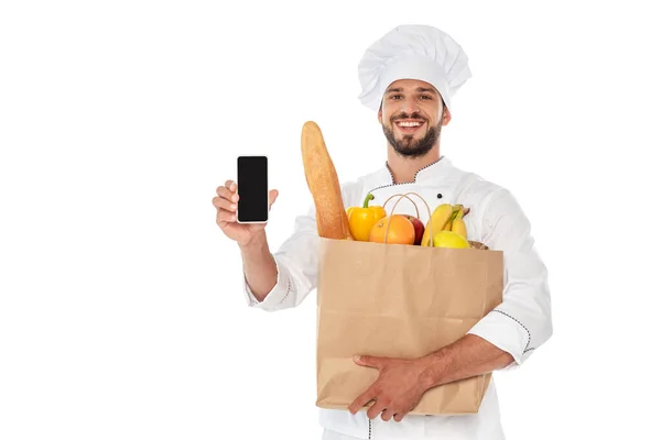 Cozinheiro sorridente segurando saco de compras com comida e smartphone isolado no branco — Fotografia de Stock