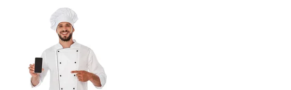 Panoramic shot of smiling chef pointing with finger at smartphone isolated on white — Stock Photo