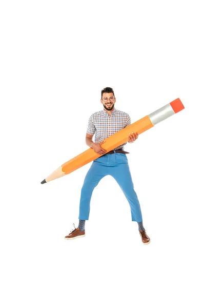 Nerd positif dans les lunettes souriant à la caméra tout en tenant un énorme crayon isolé sur blanc — Photo de stock