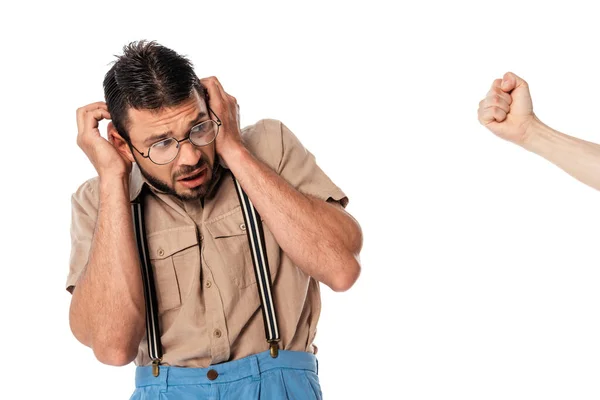 Nerd asustado en gafas que cubren las orejas cerca de puño masculino aislado en blanco - foto de stock