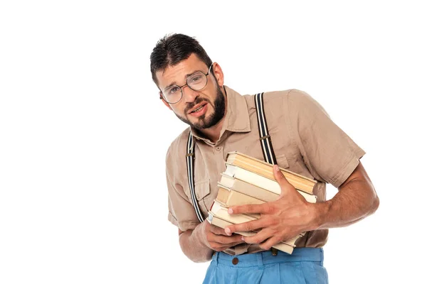 Nerd asustado en tirantes sosteniendo libros y sonriendo a la cámara aislado en blanco - foto de stock