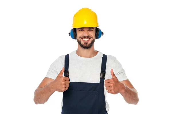 Guapo constructor sonriente en uniforme mostrando pulgares hacia arriba en la cámara aislado en blanco - foto de stock