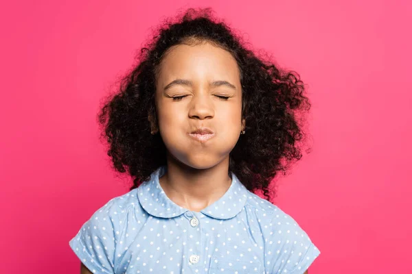 Bonito encaracolado afro-americano garoto soprando bochechas com olhos fechados isolado no rosa — Fotografia de Stock