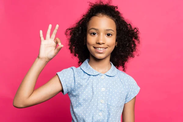 Lächelnd niedlich lockig afrikanisch amerikanischen Kind zeigt ok Zeichen isoliert auf rosa — Stockfoto