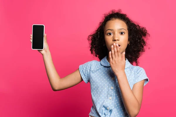 Shocked curly african american kid presenting smartphone isolated on pink — Stock Photo