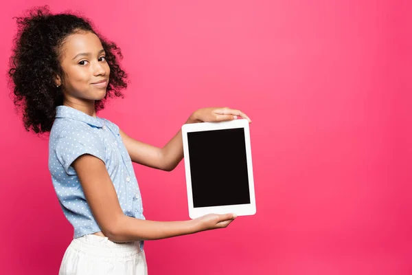 Sorrindo bonito encaracolado garoto americano africano apresentando tablet digital isolado em rosa — Fotografia de Stock