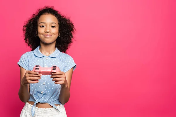 KYIV, UKRAINE - JUNE 9, 2020: smiling cute curly african american kid with joystick isolated on pink — Stock Photo