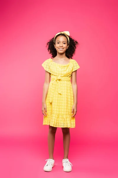 Full length view of smiling curly african american child in yellow outfit on pink background — Stock Photo