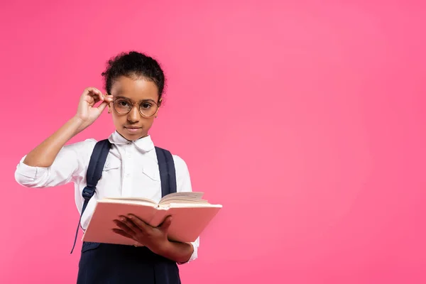 African american schoolgirl in glasses reading book isolated on pink — Stock Photo