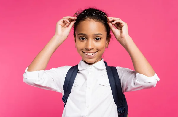 Усміхнена афроамериканська школярка регулює окуляри ізольовані на рожевому — стокове фото