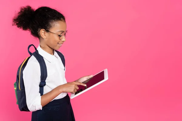 Sorrindo afro-americana estudante em óculos com mochila usando tablet digital isolado em rosa — Fotografia de Stock