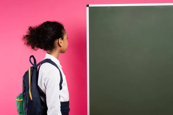 Afrikanisch-amerikanische Schülerin mit Rucksack in der Nähe leere Tafel isoliert auf rosa — Stockfoto