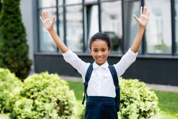 Sonriente afroamericano colegiala con mochila y manos en el aire libre - foto de stock