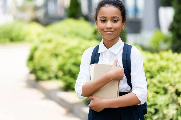 Smiling african american schoolgirl with book outdoors — Stock Photo