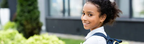 Sonriente afroamericana colegiala con mochila al aire libre, plano panorámico - foto de stock