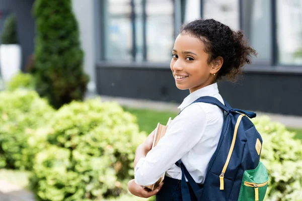 Vista laterale di sorridente studentessa afro-americana con libro all'aperto — Foto stock