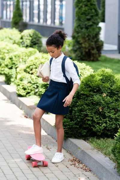 Afrikanisch-amerikanische Schulmädchen mit Rucksack und Bücher Reiten Penny Board im Freien — Stockfoto