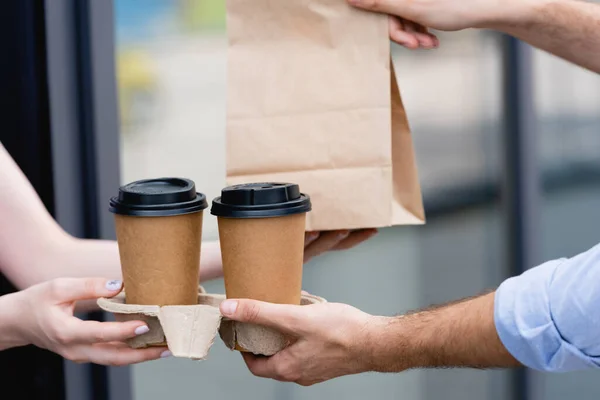 Vista cortada da garçonete dando café para ir e saco de papel para o cliente perto de café na rua urbana — Fotografia de Stock