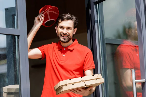 Serveur positif tenant boîtes à pizza et chapeau près du café — Photo de stock