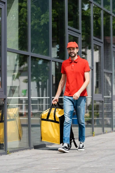 Uomo di consegna sorridente che tiene la borsa termica mentre cammina sulla strada urbana — Foto stock