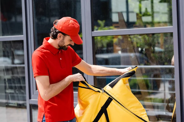 Lächelnder Kurier öffnet Thermobeutel auf urbaner Straße — Stockfoto