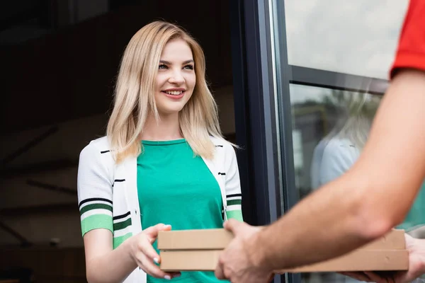 Selective focus of courier giving pizza boxes to smiling woman on urban street — Stock Photo