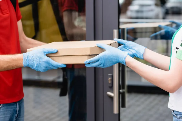 Vista cortada de correio dando caixas de pizza para mulher em luvas de látex na rua urbana — Fotografia de Stock