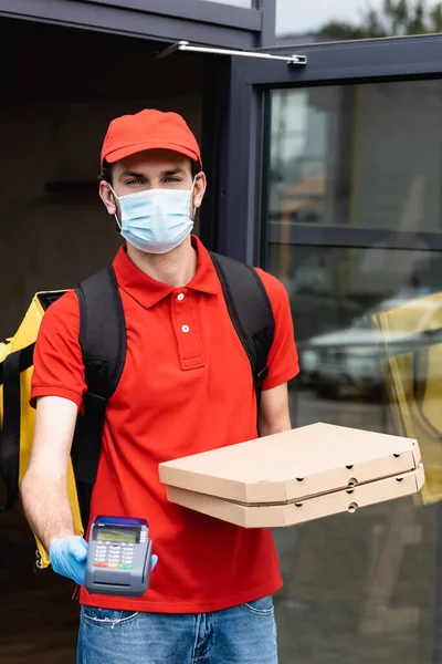 Mensajero en máscara médica y guante de látex con terminal de pago y cajas de pizza en la calle urbana - foto de stock