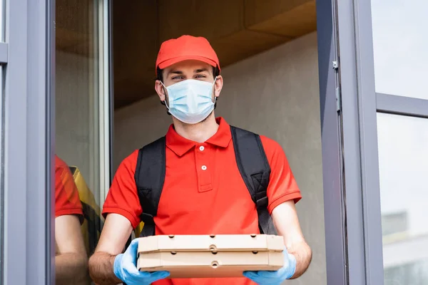 Delivery man in medical mask and latex gloves holding pizza boxes near building on urban street — Stock Photo