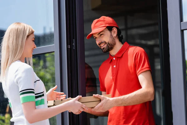 Camarero sonriente dando cajas de pizza a la mujer cerca de la cafetería en la calle urbana - foto de stock