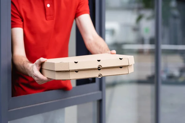 Vista recortada del camarero sosteniendo pizza para llevar cerca de la ventana del café en la calle urbana - foto de stock