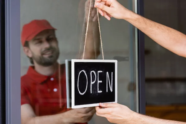 Selective focus of smiling waiter hanging signboard with open lettering on door of cafe — Stock Photo