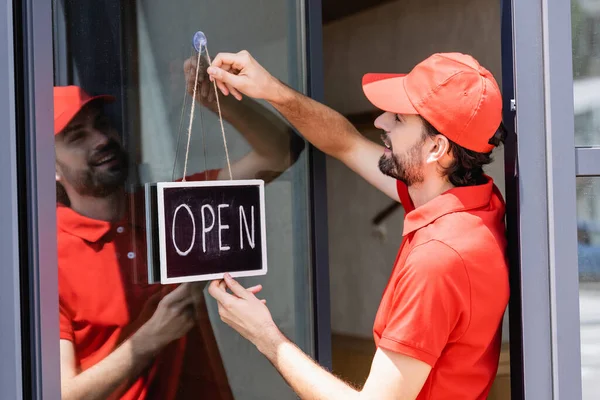 Side view of smiling waiter hanging signboard with open lettering on door of cafe — Stock Photo