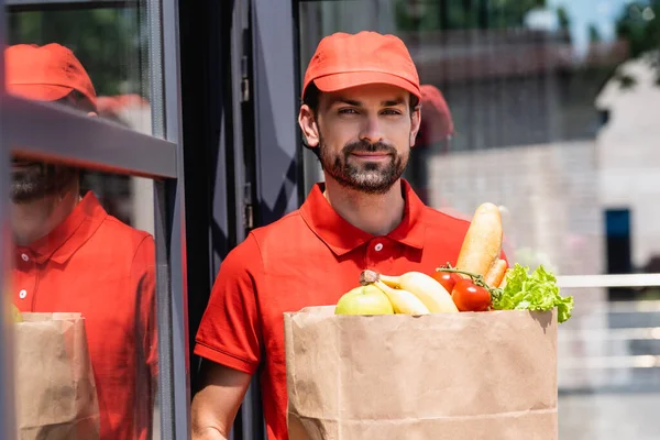 Schöner Lieferant hält Einkaufstasche mit Lebensmitteln in der Stadtstraße — Stockfoto