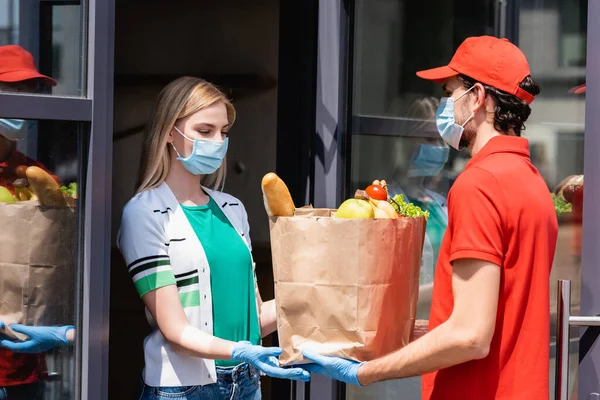 Доставка чоловік дає сумку зі свіжими фруктами та овочами жінці в медичній масці на міській вулиці — стокове фото