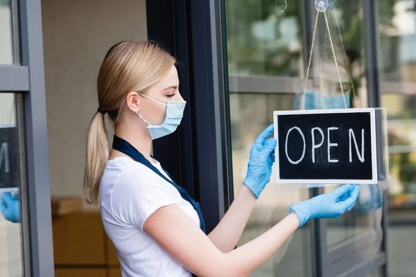 Vista laterale della cameriera appesa e guardando cartello con parola aperta sulla porta del caffè — Foto stock