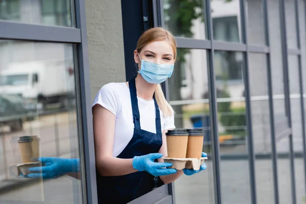 Waitress holding paper cups near window of cafe — Stock Photo