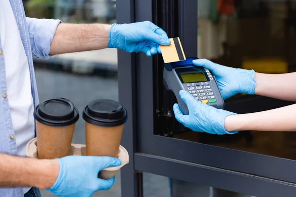 Ausgeschnittene Ansicht von Mann, der mit Kreditkarte zahlt und Kellnerin, die Zahlungsterminal in der Nähe von Café hält — Stockfoto