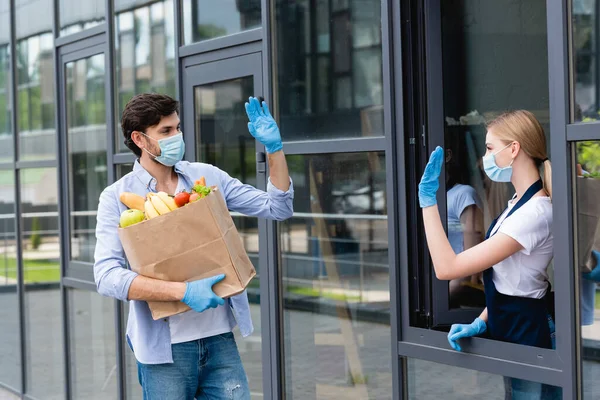 Homme tenant sac à provisions tout en agitant la main au vendeur sur la rue urbaine — Photo de stock