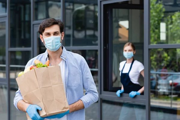 Selective focus of man holding shopping bag on urban street with architecture and saleswoman on background — Stock Photo