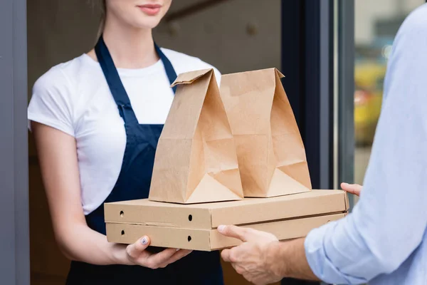 Cropped view of man receiving pizza boxes and packages from waitress near cafe — Stock Photo